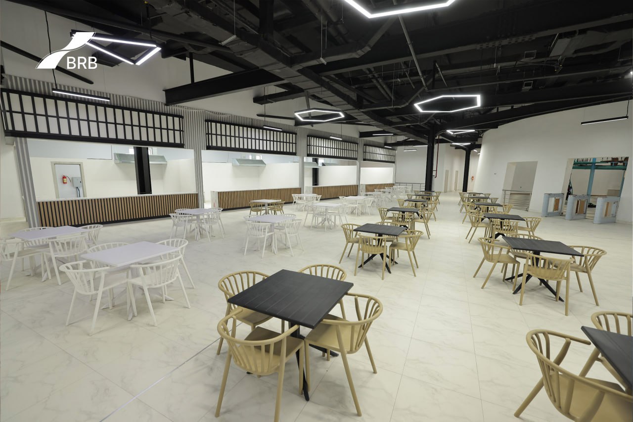 A spacious room with black metal beams, hexagonal light fixtures, and white and beige tables and chairs.