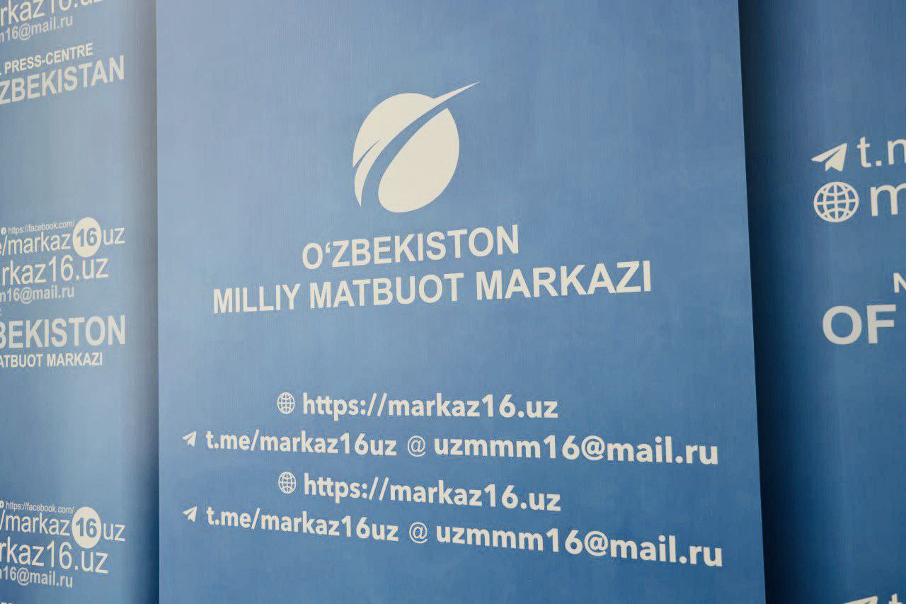 A blue sign with white text displays "O'ZBEKISTON MILLIY MATBUOT MARKAZI" and a logo, with additional text and website addresses below.